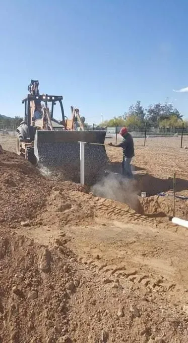 Bulldozer digging a trench on a dry construction site, with workers nearby and dust rising
