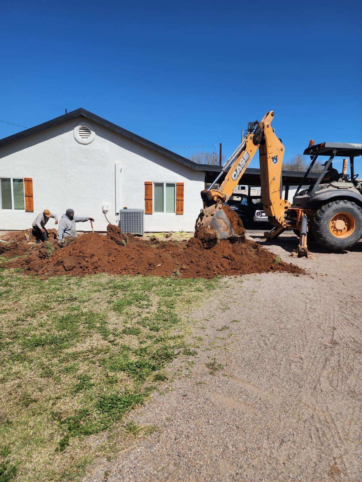 Construction workers and excavator digging along the front of a white house on a sunny day
