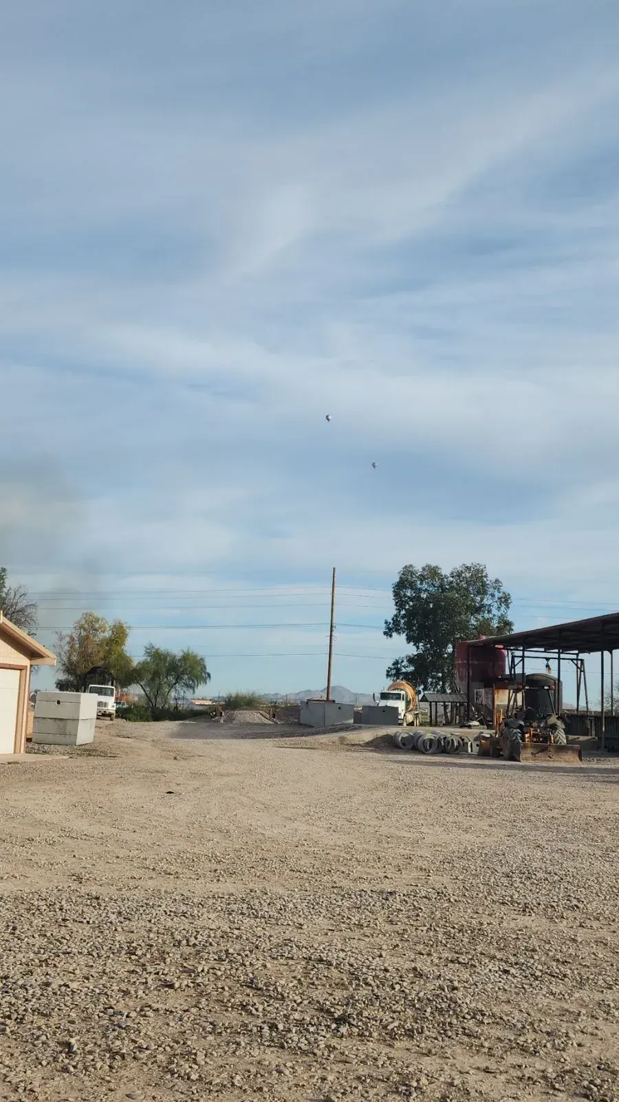 Gravel lot with a small building, utility pole, and open sky on a sunny day