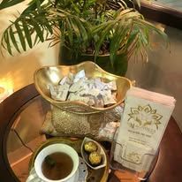 A cup of tea is sitting on a glass table next to a bowl of candy.