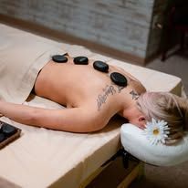 A woman is laying on a massage table with rocks on her back.