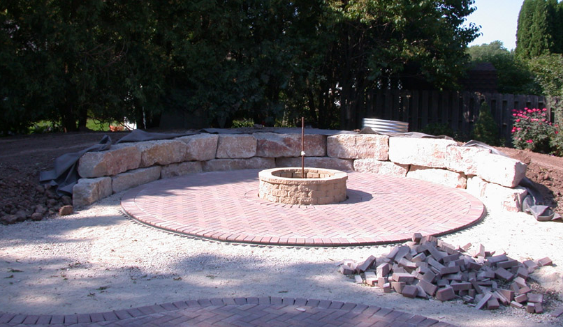 Stone fire pit in a circular patio seating area with curved stone bench and gravel ground
