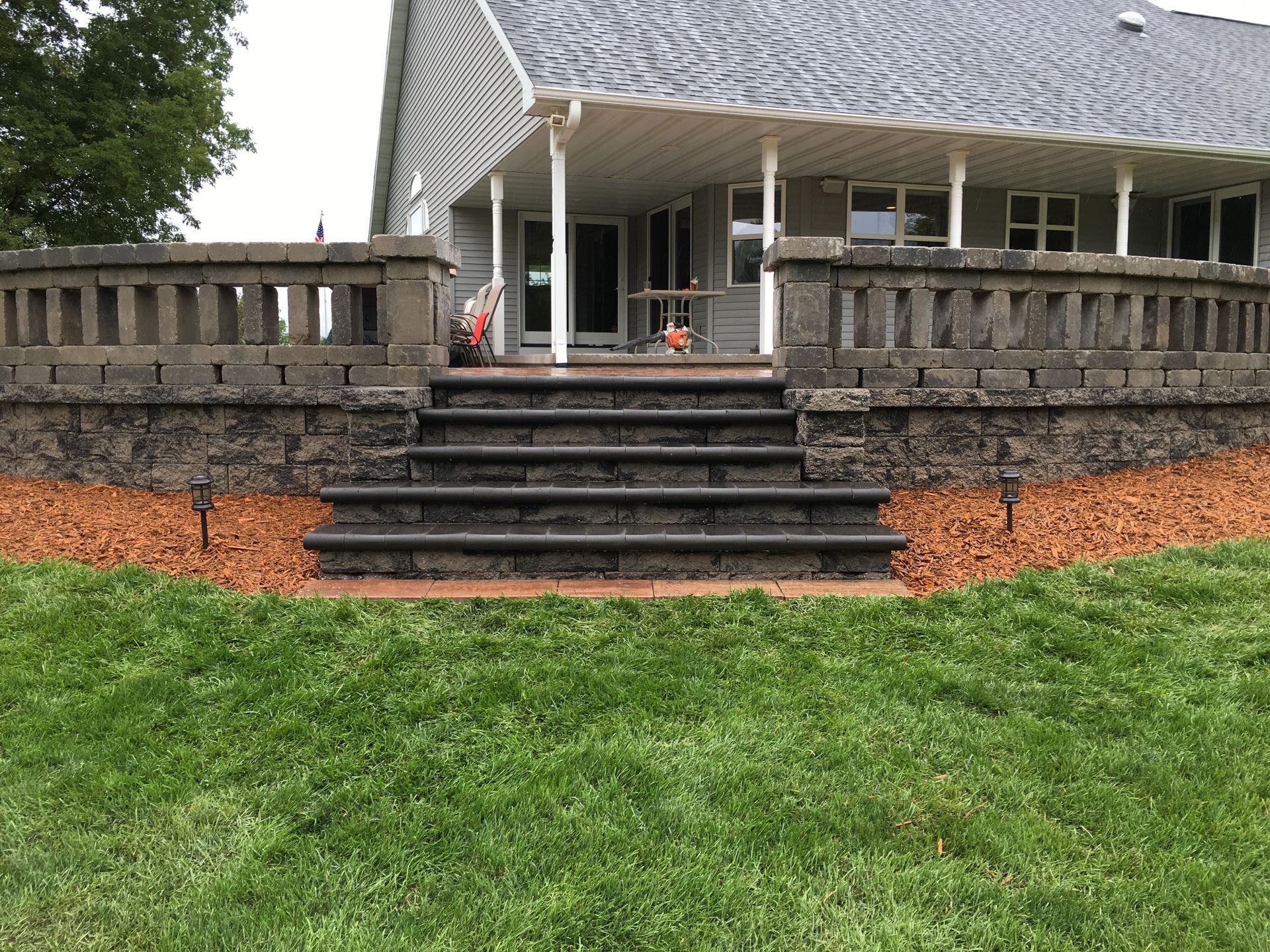 Stone patio steps leading to a covered porch on a house, with a grassy yard in front.