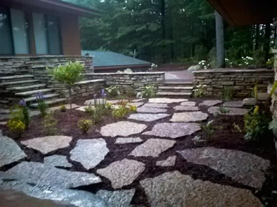 Stone walkway through a landscaped garden beside a rustic building in a wooded setting