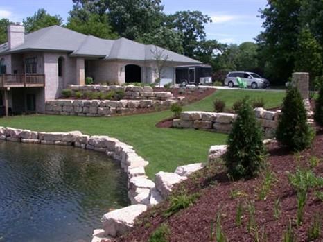 Landscaped house with stone-lined pond, lawn, and shrubs under trees