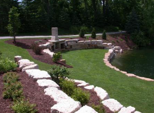 Curved stone retaining wall and landscaped lawn with rocks and shrubs in a wooded yard