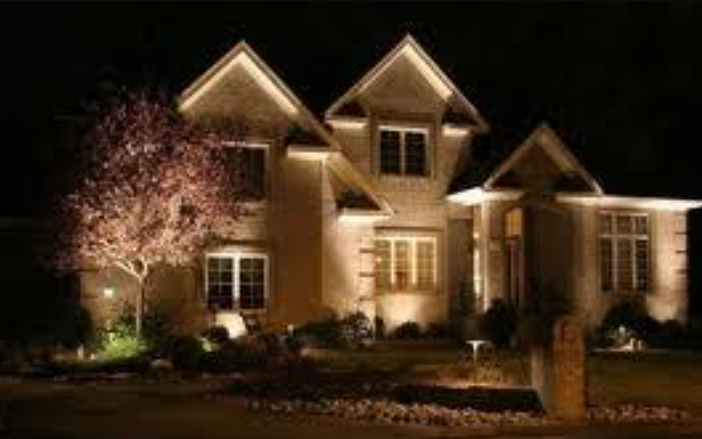 Illuminated suburban house at night with warm exterior lights and a flowering tree in front