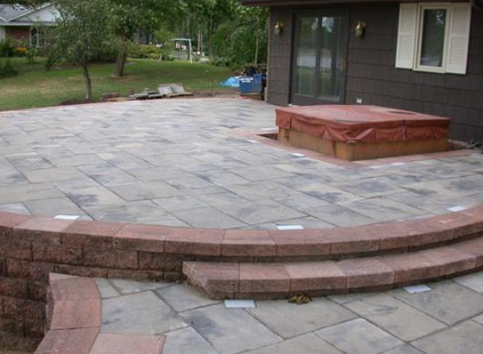 Backyard patio with stone paving, curved brick steps, and a raised wooden deck near sliding glass doors