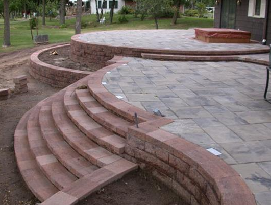 Curved brick steps and a raised stone patio in a park setting