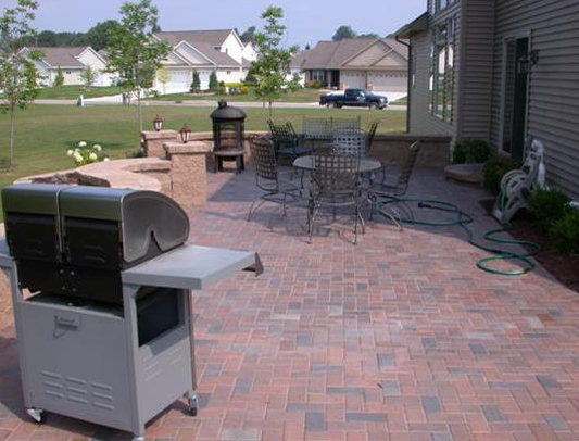 Backyard patio with grill, table, chairs, and brick pavers beside a house