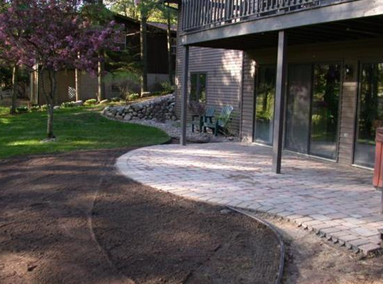 Curved paved patio beside a house with balcony and purple flowering tree in the yard