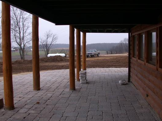 Wooden cabin porch with posts and stone patio, overlooking a bare field and distant hills