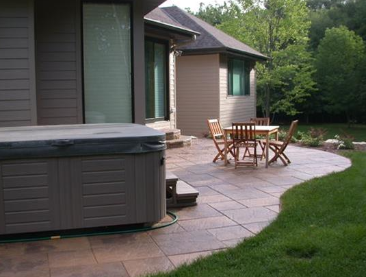 Patio with hot tub, wooden table and chairs beside a house and green lawn
