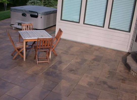 Backyard patio with a wooden table and chairs beside a hot tub and house windows
