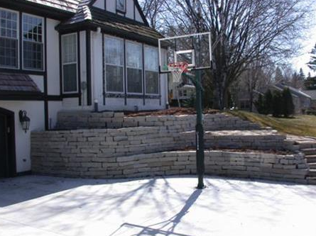 Basketball hoop on a snowy driveway beside a house with stone retaining walls