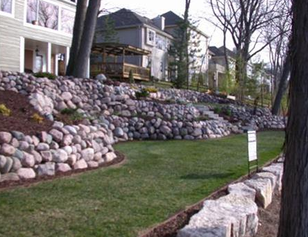 Terraced stone retaining walls beside a grassy slope in a residential neighborhood