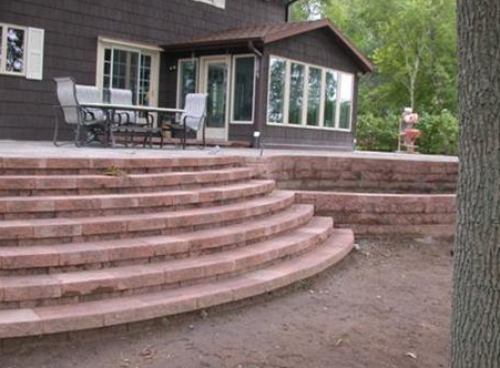 Curved stone patio steps leading to a house with a screened porch and outdoor furniture
