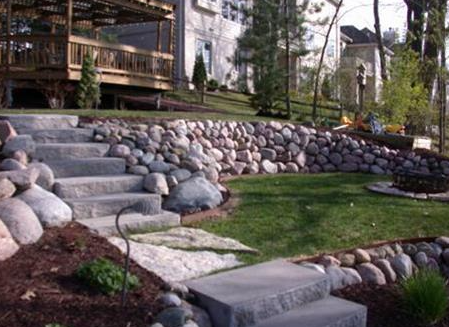 Stone steps and boulder retaining wall beside a landscaped lawn and wooden deck