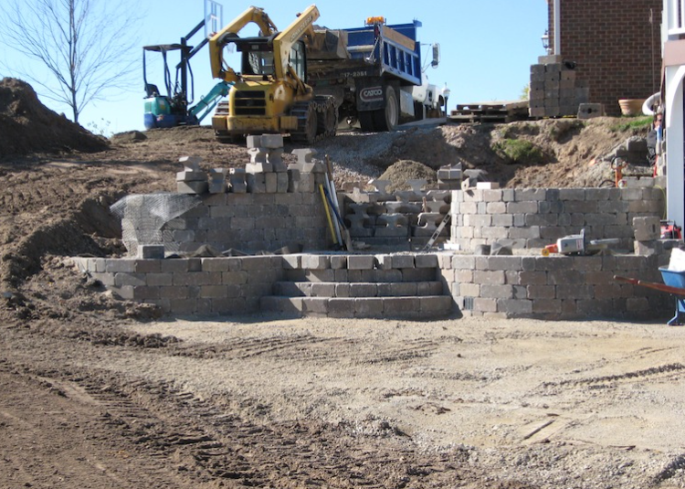 Construction site with retaining wall, steps, and heavy machinery on a dirt slope