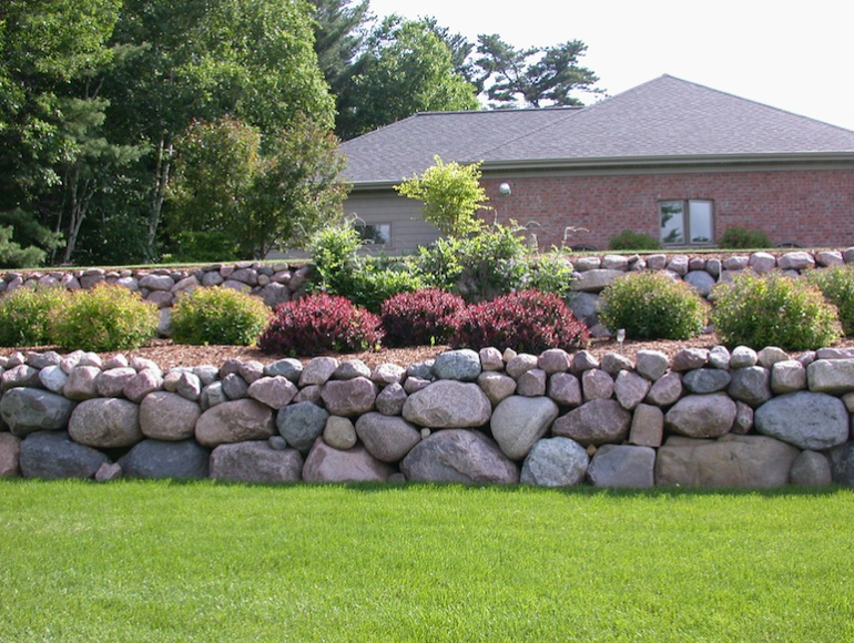 Stone terraced garden with colorful shrubs in front of a house and green lawn
