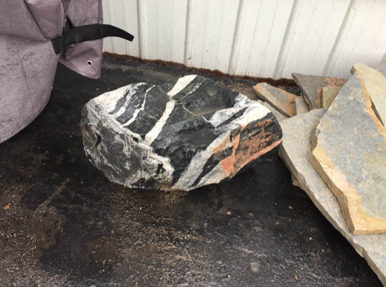 Large black-and-white striped rock on a pavement beside other stones and a wall
