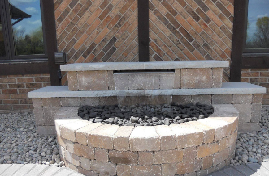 Stone outdoor fire pit with tiered seating in front of a brick wall
