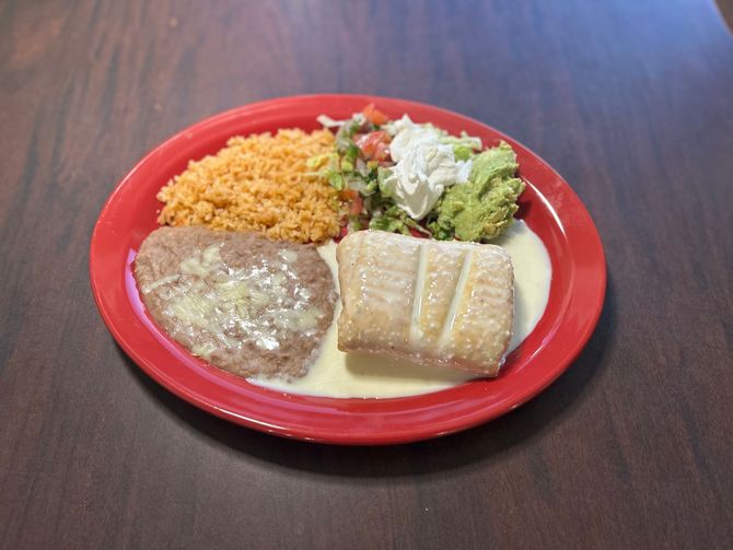 A red plate topped with rice beans and guacamole on a wooden table.