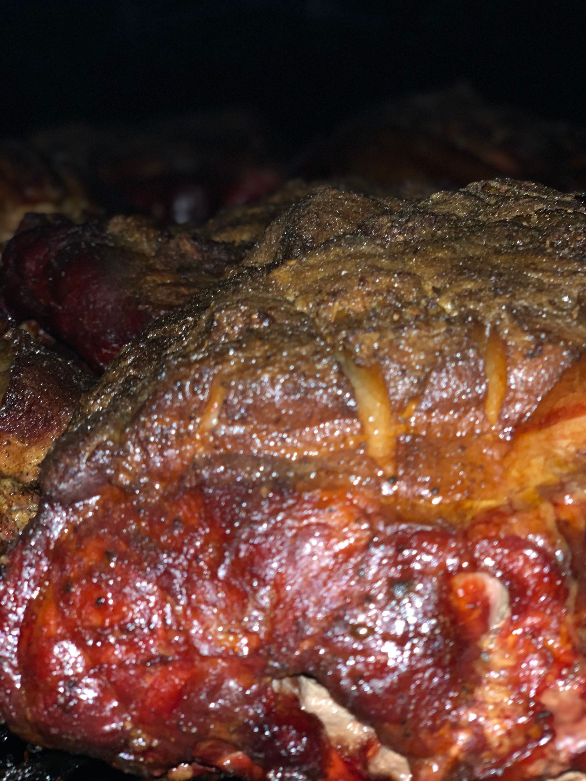 Close-up of smoked meat, showing a dark brown bark and glistening juices.
