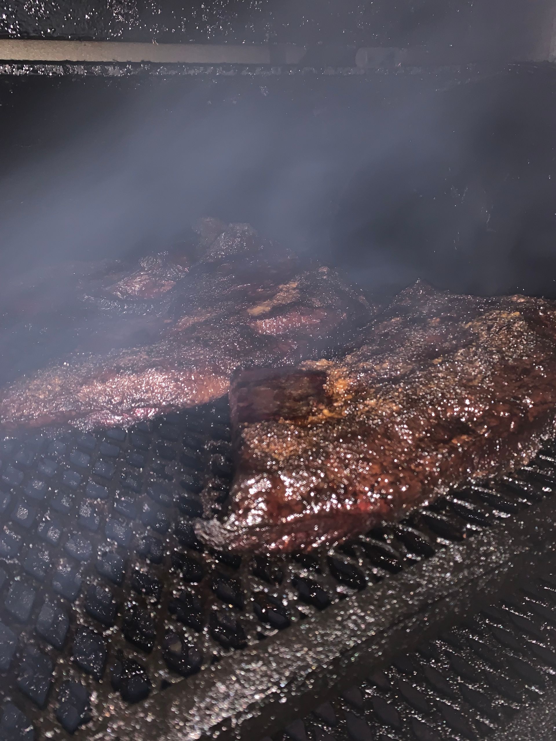 Meats smoking on a grill, surrounded by smoky haze.