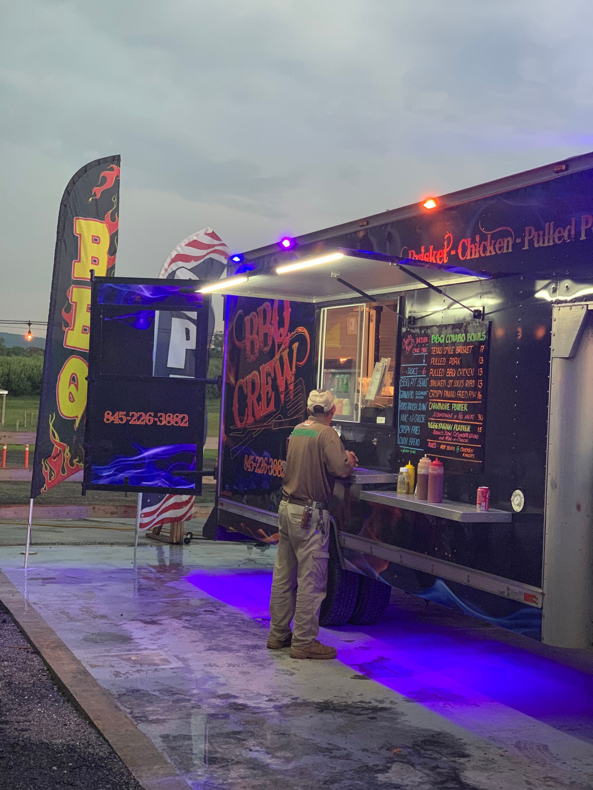 Food truck with open serving window; person in uniform prepares food under blue and white lights.