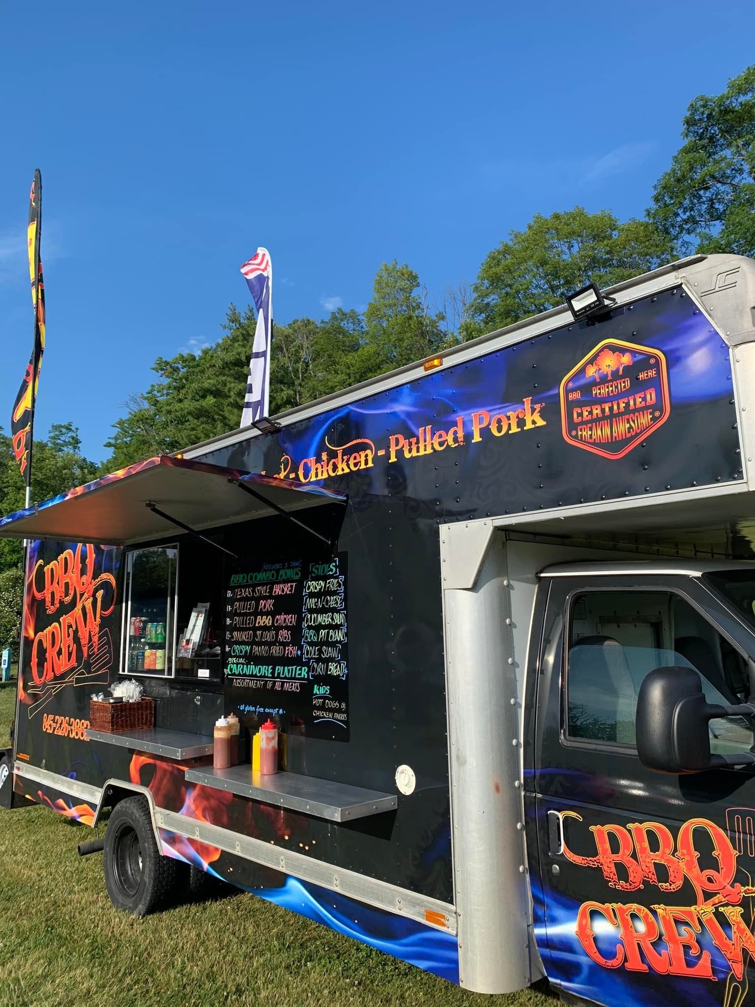 BBQ food truck with a black and orange design, parked outdoors with menu visible.