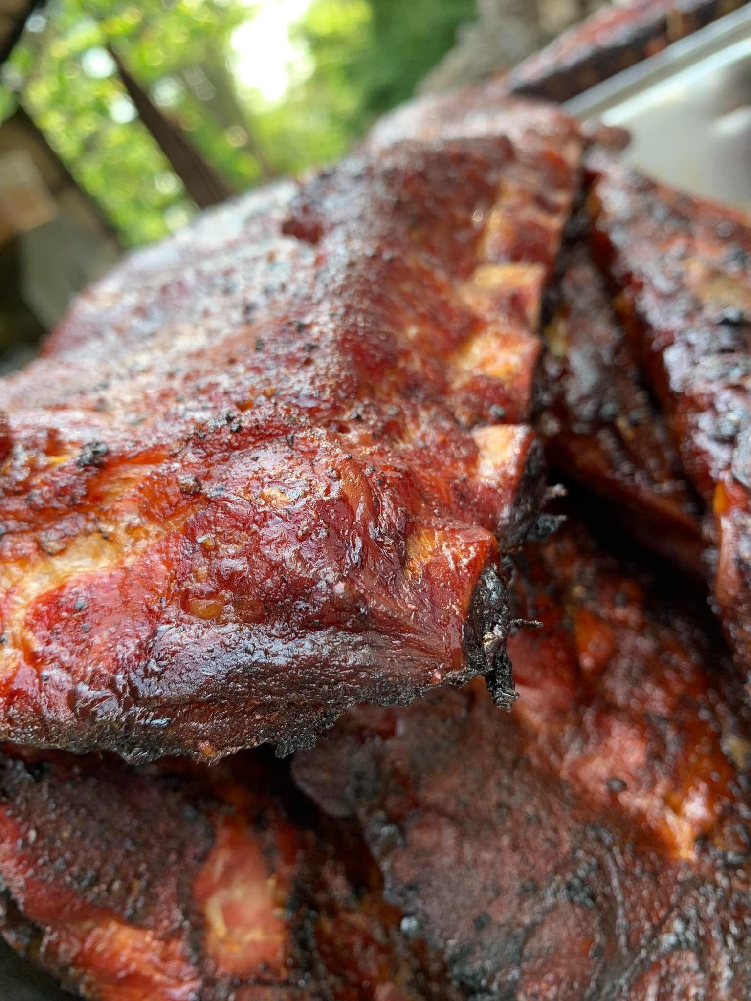Close-up of smoked ribs, deep red-brown with glossy, caramelized surface, stacked in a pile.