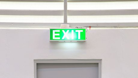 A green exit sign is hanging from the ceiling above a door.
