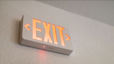 An exit sign is lit up on a white wall.