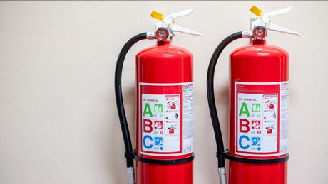 Two red fire extinguishers are hanging on a wall.
