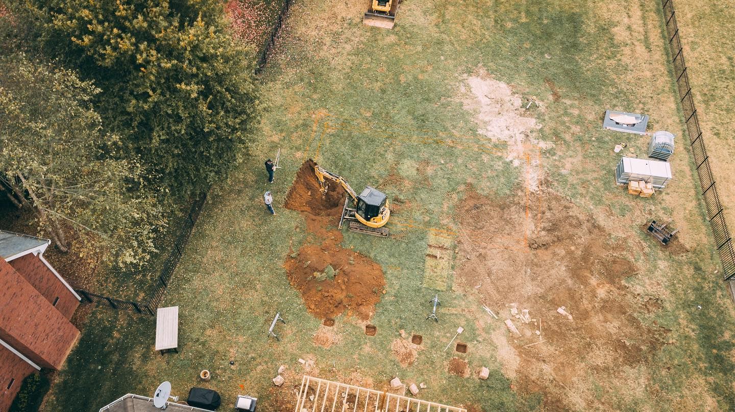 Overhead view of construction site with equipment and people digging in a grassy area.