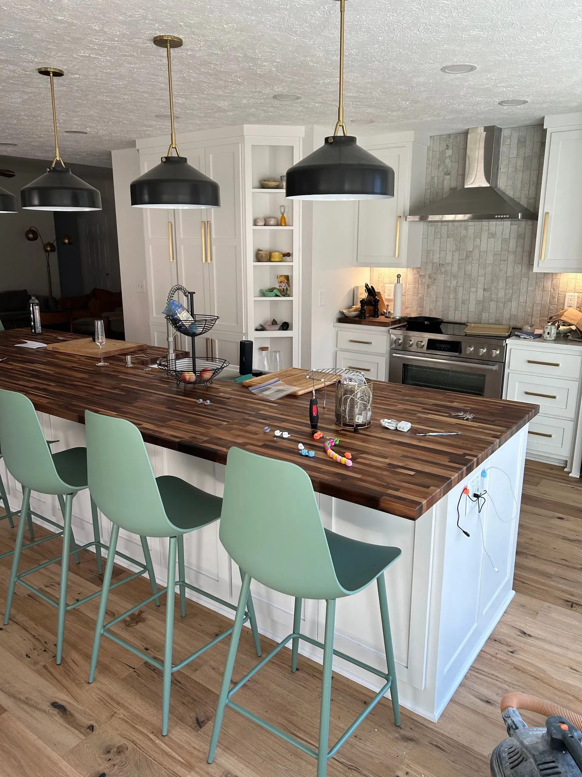 Kitchen with a wooden countertop island, green bar stools, and black pendant lights.