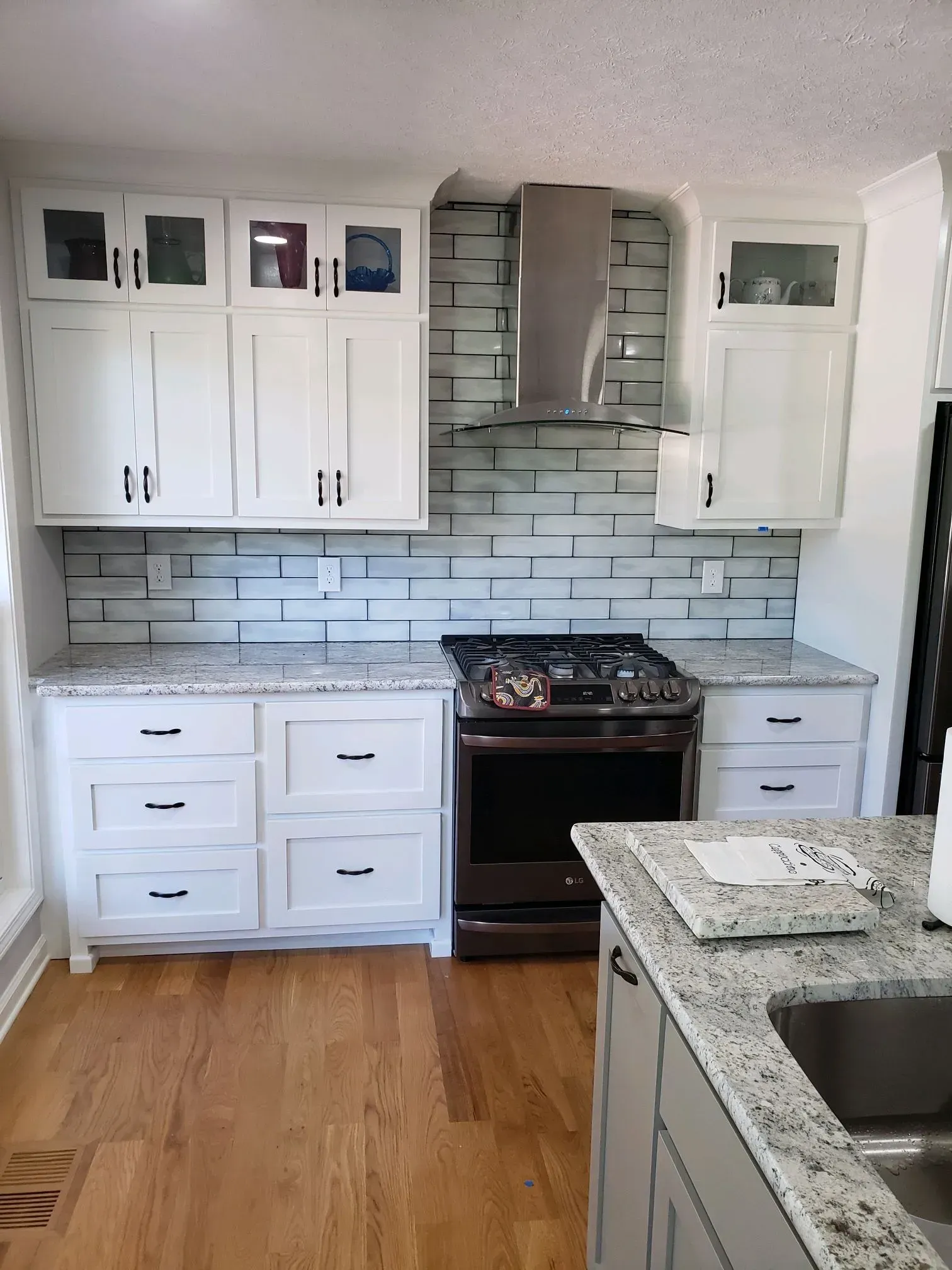 White kitchen with granite countertops and brick-style backsplash. A stove is centered with upper cabinets.