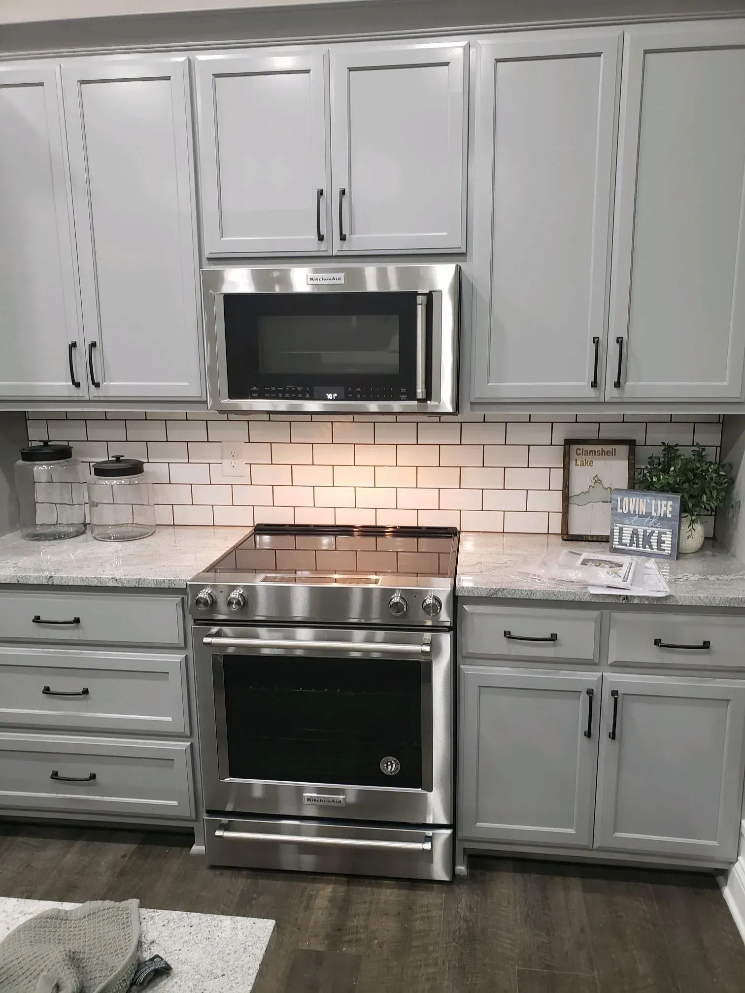 Gray kitchen cabinets with a stainless steel range and microwave, white subway tile backsplash, and light countertops.