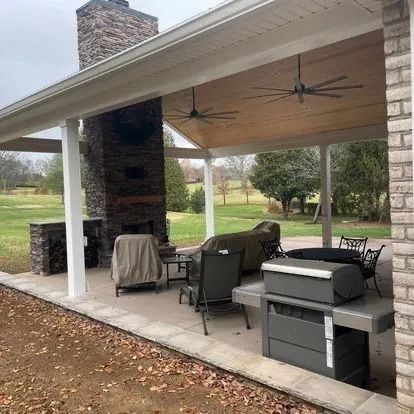 Covered patio with fireplace, grill, and seating. Overcast sky, fall leaves on ground.
