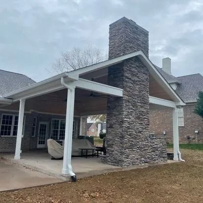 Covered outdoor patio with stone chimney, white columns, and brown ceiling.