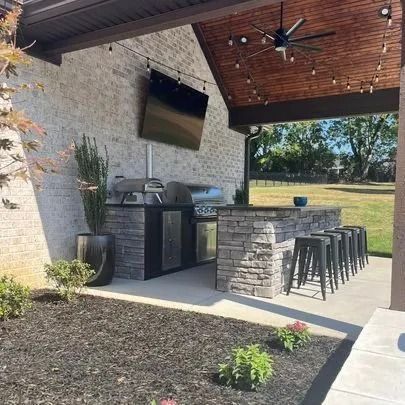 Outdoor kitchen with grill, bar, TV, seating, and string lights under a covered patio.