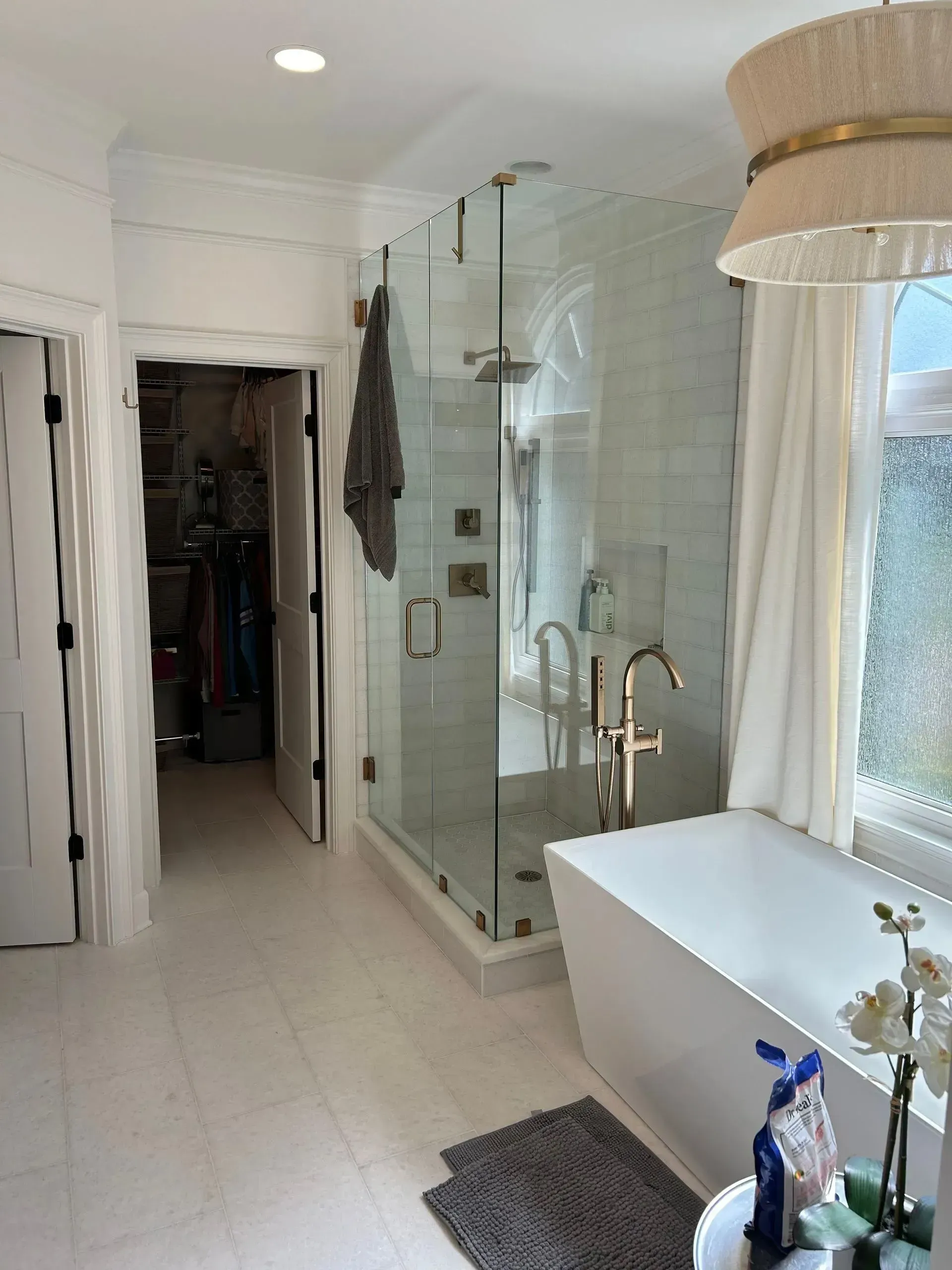 Bathroom with a glass shower, white tub, and walk-in closet. Light floors, walls, and fixtures.