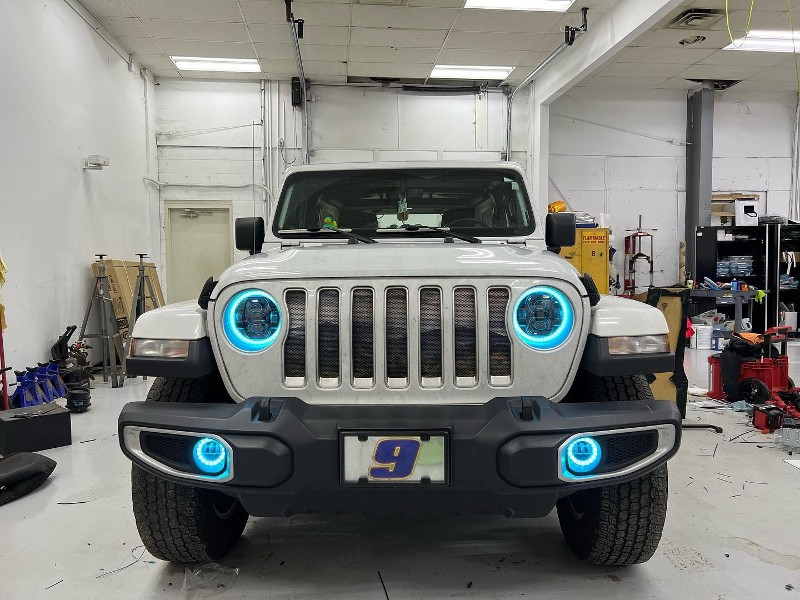 A white jeep with blue lights on the headlights is parked in a garage.