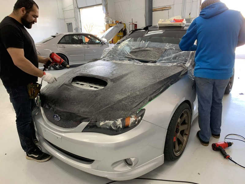 Two men are working on a white car in a garage.