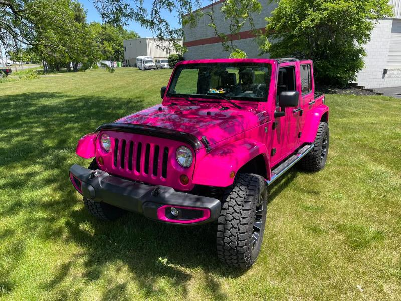 A pink jeep is parked in a grassy field.