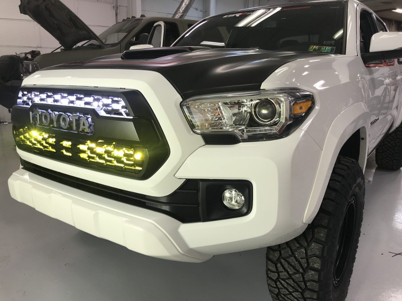 A white toyota tacoma truck with a black hood is parked in a garage.