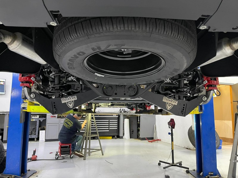 A man sits on a stool under a truck with a tire that says good year on it