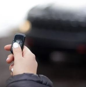 A person is holding a remote control in their hand in front of a car.