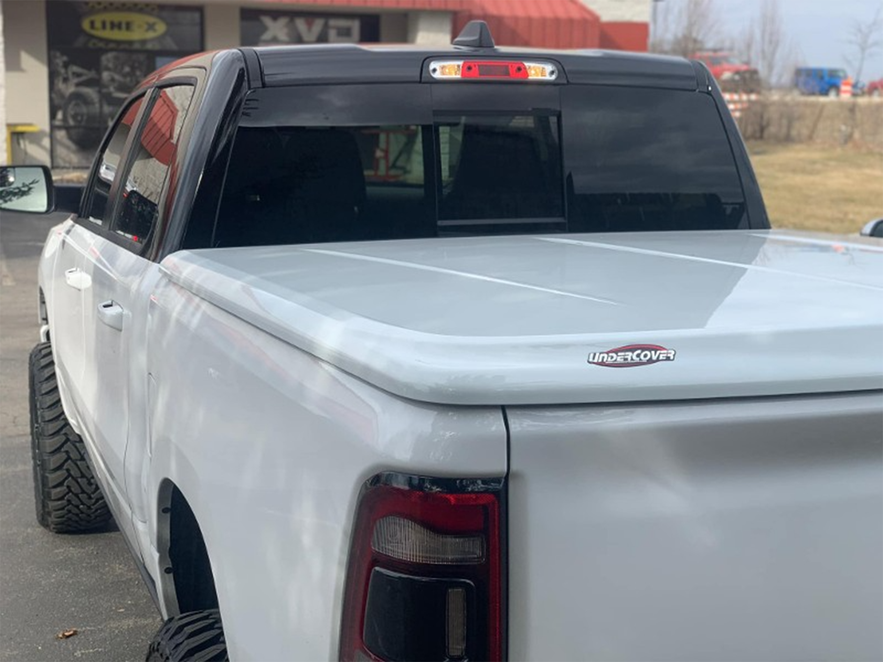 A white truck with a tonneau cover is parked in front of a building.
